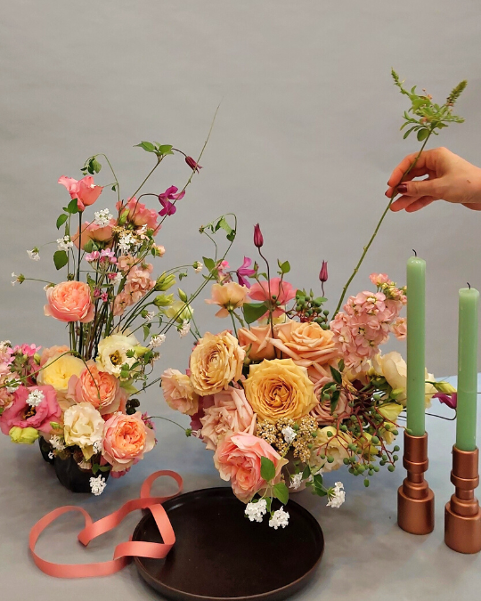 Dos composiciones florales de color pastel con una mano colocando flor